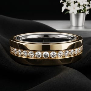 May include: A polished gold band ring featuring a central channel set with a continuous row of round brilliant-cut diamonds. The ring has a smooth, reflective metallic finish and a silver-toned interior, showcasing a classic and refined design.