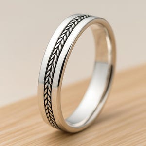 Peut inclure: Une bague argentée avec un motif tressé au centre. La bague a une finition polie et un motif détaillé. La bague est probablement en argent sterling ou en métal similaire. C'est un bijou.