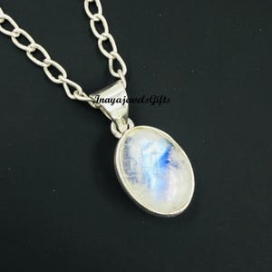 Peut inclure: Un collier en argent avec un grand pendentif ovale. Le pendentif présente une pierre de lune aux teintes bleues et blanches. La chaîne est de style maillon épais. Le texte "Inayajewels Gifts" est visible sur la bélière du pendentif.