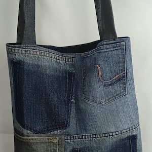 May include: A denim tote bag made from recycled jeans. The bag incorporates the original jean pockets. The straps are a dark grey fabric. A unique, eco-friendly accessory. Measurements are in centimetres.