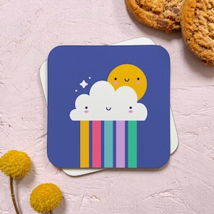 May include: A blue square coaster featuring a white cloud with a rainbow underneath. The cloud and sun have smiling faces. The sun is yellow and the rainbow is red, orange, yellow, green, blue, purple.