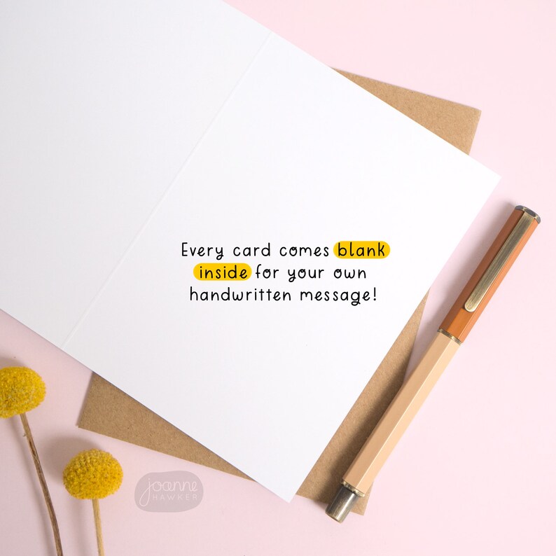 May include: A blank greeting card with the text "Every card comes blank inside for your own handwritten message!" printed on the inside. The card is on a pink surface with a brown envelope and a pen.