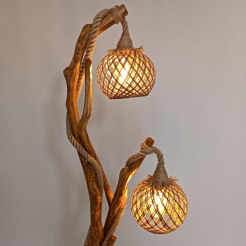 Peut inclure: Un lampadaire rustique avec une structure en bois naturel et deux abat-jours globes tiss&eacute;s. La lampe pr&eacute;sente un design enroul&eacute; de corde et une lumi&egrave;re chaleureuse et invitante. La hauteur de la lampe est d'environ 152 cm.