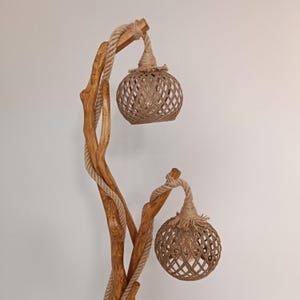 Peut inclure: Un lampadaire rustique avec une structure en bois naturel et deux abat-jours globulaires tress&eacute;s. La lampe pr&eacute;sente un d&eacute;tail de corde torsad&eacute;e et une esth&eacute;tique chaleureuse. La hauteur de la lampe est d'environ 152 cm.