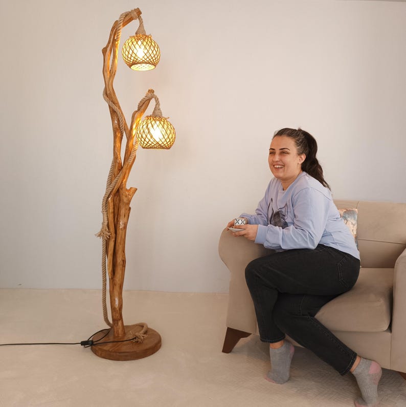 Peut inclure: Un lampadaire rustique avec une base en bois naturel et une structure en forme d'arbre. Deux abat-jours globes en rotin tress&eacute; sont suspendus aux branches. La lampe est envelopp&eacute;e de corde et poss&egrave;de une base ronde en bois.