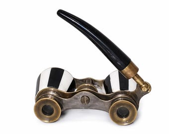 May include: Antique opera glasses with a black handle and brass accents. The lenses are framed in a silver-toned metal, and the eyepieces feature a black and white striped design. A classic accessory for theater or events.