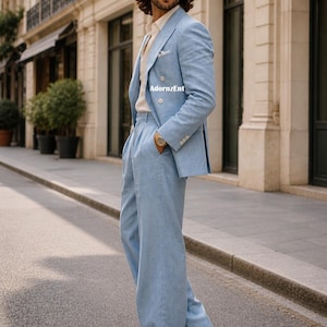 May include: A light blue linen suit with a double-breasted blazer and wide-leg pants. The suit is paired with a cream-colored shirt and white shoes. The image is taken outdoors on a city street.
