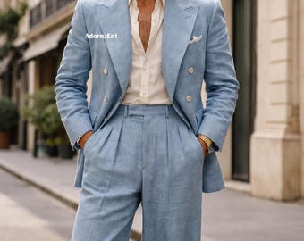 May include: A pale blue double-breasted suit with matching wide-leg trousers. The suit is worn over a cream-coloured button-down shirt. The image is taken outdoors on a city street. The suit has a pocket square and gold watch.