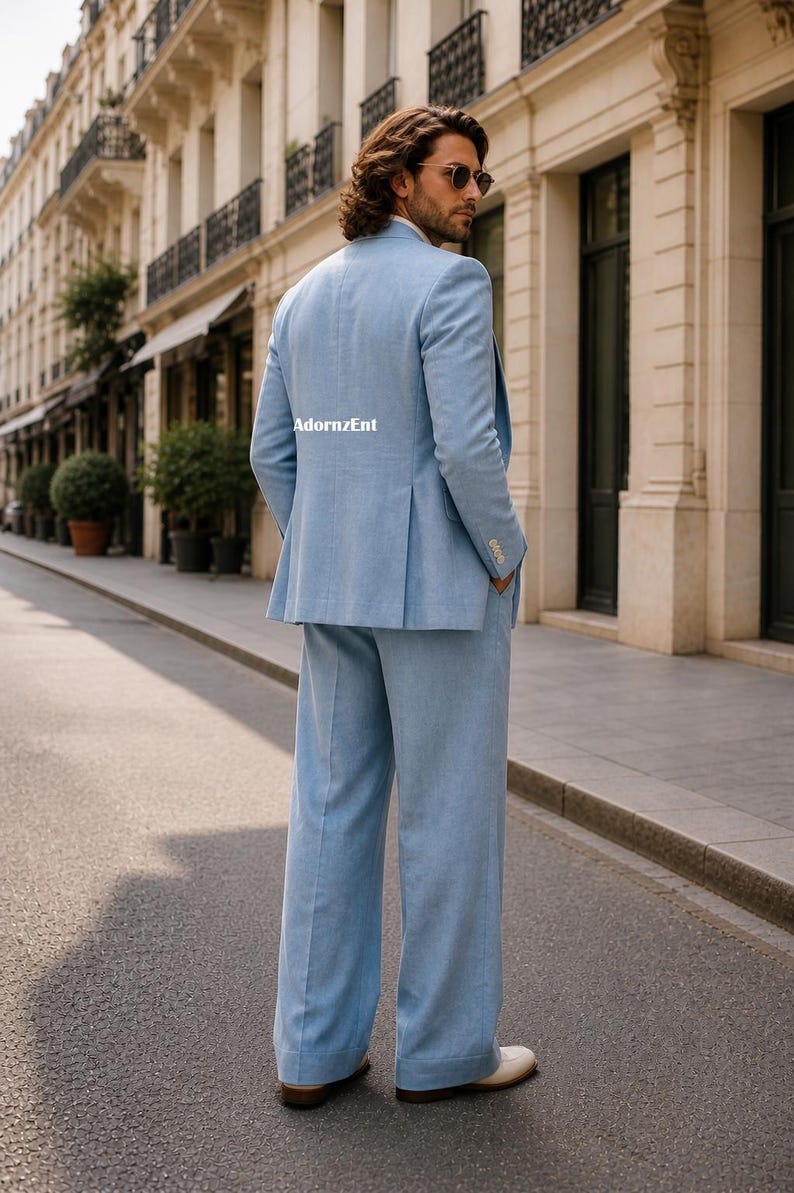 May include: A light blue suit with wide-leg pants. The suit jacket has a classic design with a notched lapel and a two-button closure. The pants are a wide-leg style. The suit is worn with white shoes. The text "AdornzEnt" is visible on the jacket.