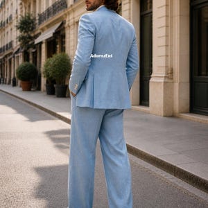 May include: A light blue suit, including a blazer and wide-leg pants, is worn by a person standing on a city street. The suit is paired with white shoes. The text "AdornzEnt" is visible on the back of the blazer.