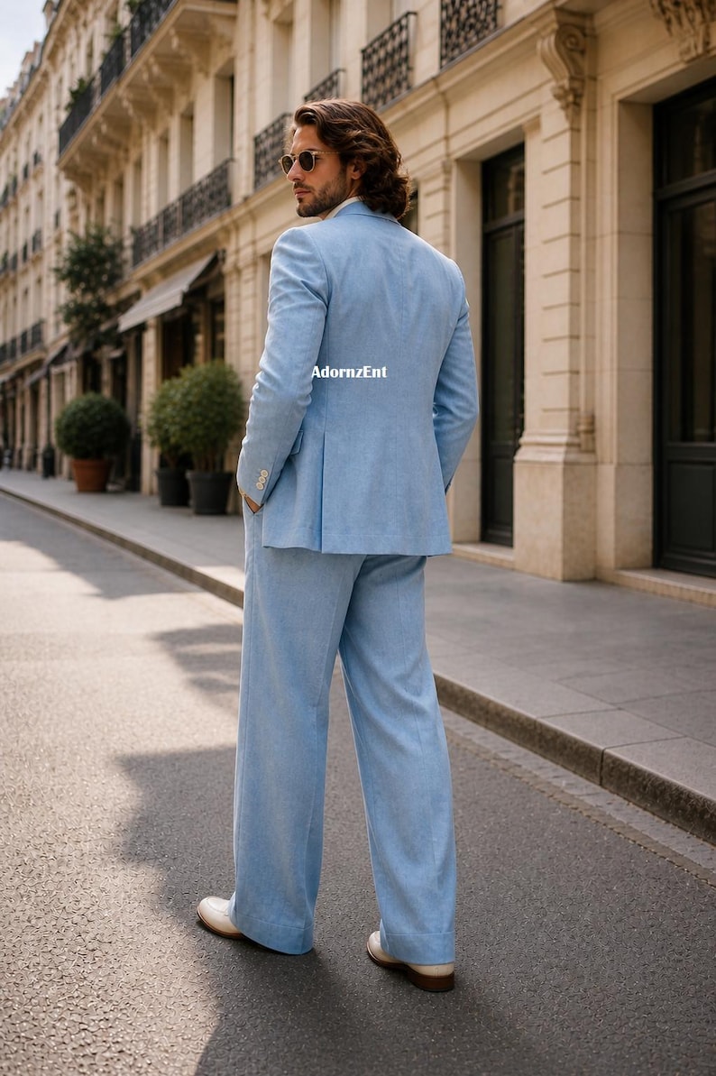 May include: A light blue suit, including a blazer and wide-leg pants, is worn by a person standing on a city street. The suit is paired with white shoes. The text "AdornzEnt" is visible on the back of the blazer.