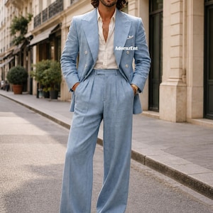 May include: A light blue linen suit, featuring a double-breasted blazer and wide-leg trousers. The suit is paired with a white button-down shirt and white loafers. The outfit is completed with sunglasses and a gold watch. The image is taken outdoors.