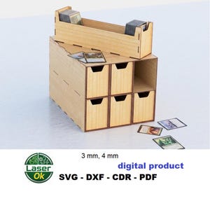 Peut inclure: Un organisateur de rangement en bois clair avec six tiroirs et un plateau supérieur, conçu pour les cartes à collectionner. Le texte 3 mm, 4 mm, digital product, SVG - DXF - CDR - PDF est visible. Plusieurs cartes sont placées dedans et autour.