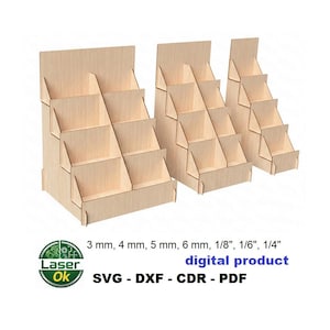 Op de afbeelding: Drie houten display stands van verschillende formaten, elk met meerdere trapsgewijze planken. De stands zijn gemaakt van lichtgekleurd hout en zijn ontworpen om kleine items te tonen. De afbeelding bevat tekst: "3 mm, 4 mm, 5 mm, 6 mm, 1/8", 1/6", 1/4" digitaal product SVG - DXF - CDR - PDF".
