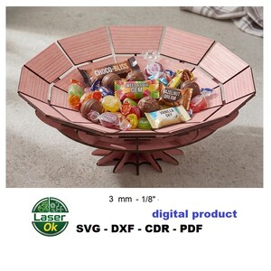 May include: A pink, multi-paneled, circular wooden bowl with a star-shaped base, filled with assorted wrapped candies and chocolate bars. The text 3 mm - 1/8" and digital product SVG - DXF - CDR - PDF is visible below the bowl.