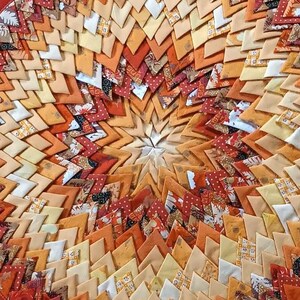 Könnte beinhalten: Ein runder, handgefertigter Topfuntersetzer mit einem lebendigen, geometrischen Design. Der Untersetzer zeigt ein Spiralmuster aus orangefarbenen, gelben und cremefarbenen Stoffstücken, umrahmt von einem roten Rand. Dieser dekorative Artikel schützt Oberflächen.