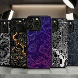 May include: A collection of five black phone cases with topographic map designs. The cases feature vibrant colors, including black and white, gold, purple, and blue. The cases are displayed on a gray surface.