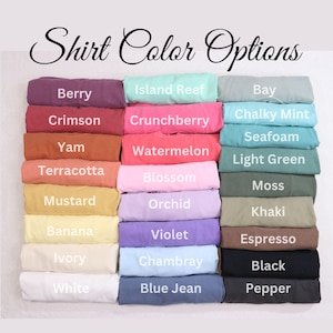 May include: A display of folded shirts in various colors, including Berry, Crimson, and Yam. The image features the text "Shirt Color Options" in a decorative font, showcasing a range of hues from pastels to darker shades.