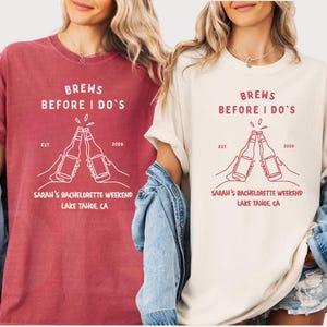 May include: Two t-shirts, one red and one cream, with the text "BREWS BEFORE I DO'S" and "SARAH'S BACHELORETTE WEEKEND LAKE TAHOE, CA" in white. The design includes two beer bottles clinking together.