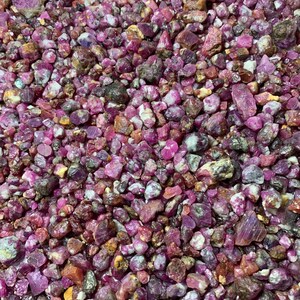 以下が含まれることがあります： 未加工のルビーの原石の山をクローズアップ。石はサイズと形状が異なり、ピンク、赤、茶色の色合いを示しています。宝石は自然で未研磨の外観をしています。