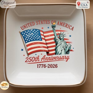 Könnte beinhalten: Eine quadratische weiße Keramikschale mit goldfarbenem Rand, verziert mit einer amerikanischen Flagge und der Freiheitsstatue. Der Text lautet UNITED STATES OF AMERICA, 250th Anniversary und 1776-2026, ergänzt durch kleine blaue und rote Sterne.
