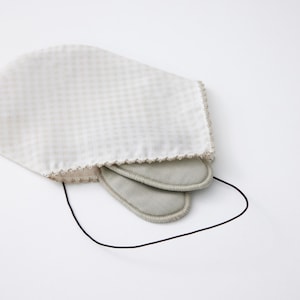 Op de afbeelding: Een wit slaapmasker met een ruitpatroon en geschulpte rand, met twee grijze oogpads. Een zwart elastisch koord is bevestigd. Het masker is ontworpen om licht te blokkeren.