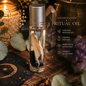 Könnte beinhalten: Eine klare Glas-Roll-On-Flasche mit silbernem Verschluss, die Flüssigkeit, ein getrocknetes Blatt und dunkle Steine enthält. Der Text auf dem Bild lautet: HANDCRAFTED RITUAL OIL, NATURAL BOTANICALS, CRYSTAL INFUSED, MADE WITH INTENTION, ENERGY ACTIVATED.