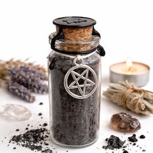 Puede incluir: Un frasco de vidrio transparente lleno de gránulos de color gris oscuro, coronado con un corcho y un sello de cera negro. Un colgante de pentagrama plateado cuelga del frasco. El fondo incluye lavanda seca, una vela encendida y cristales.