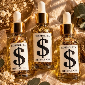 Könnte beinhalten: Drei klare Glastropfflaschen gefüllt mit goldenem Öl und getrockneten Kräutern. Jede Flasche hat ein weißes Etikett mit dem Text COSMOLITA, einem großen schwarzen Dollarzeichen und den Worten RITUAL OIL in schwarzen Großbuchstaben.