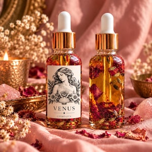Könnte beinhalten: Zwei klare Glastropfflaschen gefüllt mit goldenem Öl, getrockneten Rosenblättern und Lavendelknospen. Eine Flasche hat ein weißes Etikett mit einer schwarz-weißen Illustration, dem Text VENUS und dem Markennamen COSMOLITA darunter.