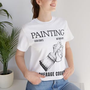 May include: White t-shirt with the word "PAINTING" in large black letters. Below the word "PAINTING" are the words "EVEN COATS" and "NO TOUCH-UPS". A graphic of a paintbrush and paint can is below the text. The words "AVERAGE COUNTS" are at the bottom.