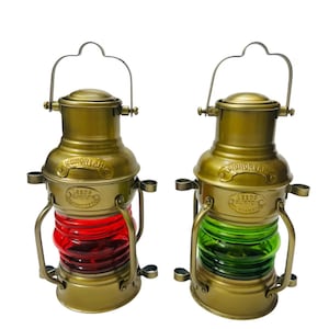 Puede incluir: Dos faroles náuticos de color latón con lentes de vidrio. Un farol tiene una lente roja, el otro una lente verde. Cada farol tiene un asa y el texto "LEEDS & BURTON" y "ANCHOR LAMPS".