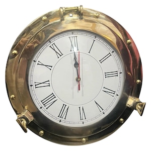 May include: A circular wall clock featuring a polished brass porthole frame with decorative rivets. The white clock face displays black Roman numerals and thin black hour and minute hands, complemented by a slender red second hand.