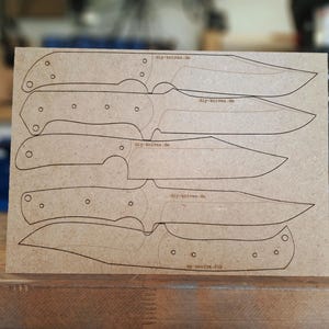 Può includere: Un pezzo di cartone color marrone con diversi modelli di coltelli disegnati con inchiostro nero. Il sito web "diy-knives.de" è stampato sul cartone. I modelli di coltelli variano per forma e dimensione.