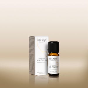 Könnte beinhalten: Eine kleine bernsteinfarbene Glasflasche mit schwarzem Verschluss neben einer weißen Schachtel. Beide tragen die Aufschrift "Relaqz selfcare" und "Anti-Stress". Die Flasche enthält Flüssigkeit, und die Schachtel hat deutschen Text. Der Hintergrund ist ein hellbrauner Farbverlauf.