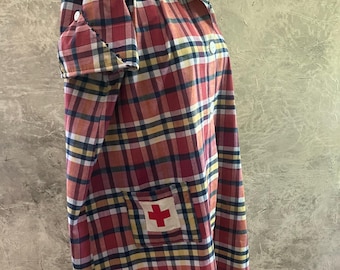 May include: A vintage-style, long-sleeved plaid shirt in red, yellow, blue, and white. The shirt features a collar, button closures, and a pocket with a red cross emblem. The shirt is displayed on a mannequin.
