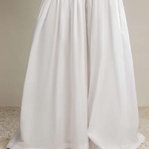 Puede incluir: Una prenda blanca y fluida, con cintura fruncida y perneras anchas y acampanadas. La tela cae elegantemente, creando una silueta voluminosa. La prenda está hecha de un material ligero, ideal para el calor.