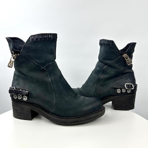 May include: A pair of dark teal leather ankle boots. The boots have a distressed appearance, with a zipper on the side and a buckle detail around the ankle. The heels are approximately 2 inches high.