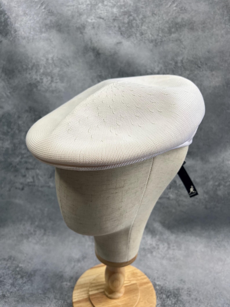 Puede incluir: Un sombrero tipo boina blanco, texturizado, con una corona redondeada y un ala corta. El sombrero se exhibe en una cabeza de maniqu&iacute;. El sombrero tiene un patr&oacute;n sutil y un ribete en contraste. Una etiqueta negra est&aacute; adherida al sombrero.