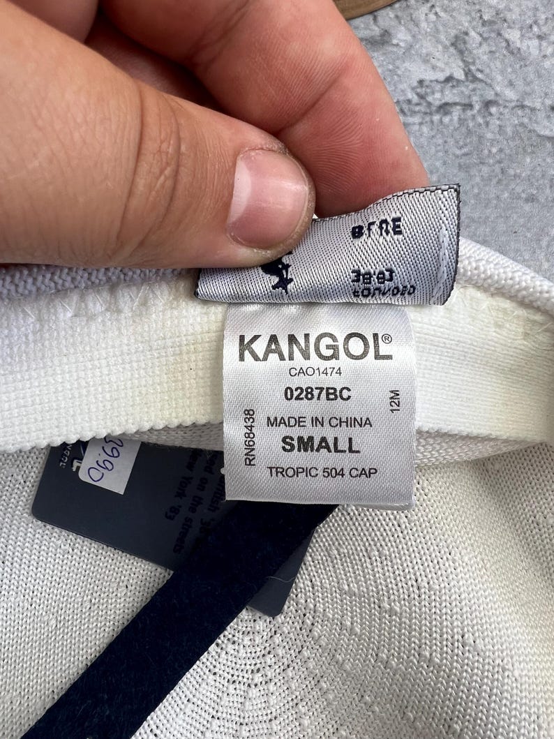 Puede incluir: Primer plano de la etiqueta de una gorra Kangol Tropic 504 blanca y blanquecina. La etiqueta dice "KANGOL" y "SMALL". Una etiqueta de precio con el n&uacute;mero "39.90" es visible. La gorra est&aacute; hecha en China.