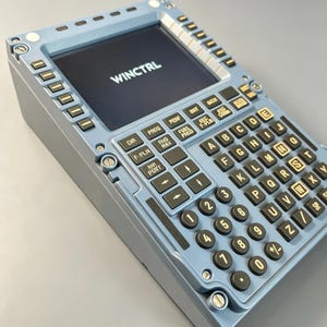 Könnte beinhalten: Ein hellblaues Flugmanagementsystem-Steuergerät mit einem rechteckigen Bildschirm, der den Text WINCTRL anzeigt. Das Gerät verfügt über einen Ziffernblock, eine alphabetische Tastatur und verschiedene Funktionstasten mit schwarzen Tasten und weißer Schrift.