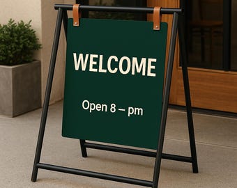 May include: A-frame sign with a dark green chalkboard displaying the word "WELCOME" in white, with "Open 8 - pm" below. The sign is held by a black metal frame with brown leather straps.