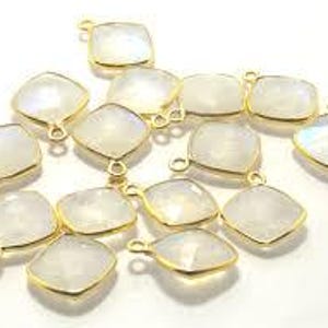Könnte beinhalten: Eine Sammlung quadratischer Anhänger mit durchscheinenden, milchig-weißen Edelsteinen in goldfarbenen Metallfassungen. Jeder Anhänger verfügt über einen kleinen runden Ring an der Oberseite zur Befestigung und weist eine glatte, facettierte Oberfläche auf.