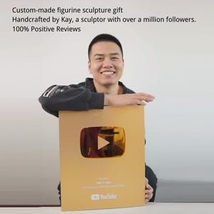 以下が含まれることがあります： 大きな金色のYouTube再生ボタンアワードを持つ人物。アワードには再生ボタンのシンボルとYouTubeのロゴがあります。アワードのテキストには「Kay's Play」と「100％ポジティブレビュー」と書かれています。