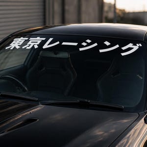 Peut inclure: Un pare-brise de voiture noir arborant un autocollant en vinyle blanc avec le texte japonais Tokyo Racing dans une police sans empattement grasse. L'autocollant est appliqué horizontalement sur la partie supérieure de la vitre du véhicule.