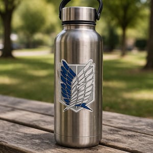 May include: A silver-coloured water bottle with a black handle. The bottle has a blue and white emblem on a grey background. It is on a wooden bench in a park, with trees in the background.