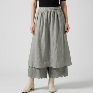 Puede incluir: Una falda de lino gris claro y pantalones cortos a juego con dobladillo festoneado. El conjunto se combina con una camiseta negra de manga corta y botines color crema. La falda tiene cintura elástica.