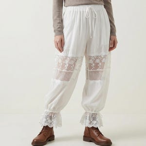 Puede incluir: Pantalones blancos con cordón, paneles de encaje y puños con volantes. Los pantalones tienen un corte holgado y están hechos de una tela ligera. La modelo lleva botas marrones. Una opción elegante y cómoda para ropa informal.