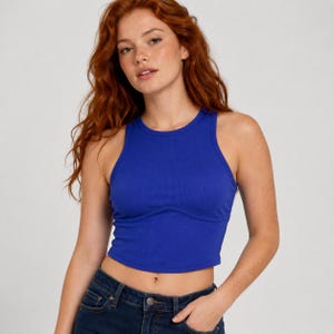 Puede incluir: Una camiseta sin mangas de canalé en color azul real con un detalle de costura curva en la zona del pecho. La prenda es de corte corto y está confeccionada con un tejido texturizado, ofreciendo una silueta ajustada sobre la cintura.