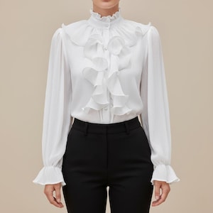 以下が含まれることがあります： ハイネックの白いブラウス。フロントにはフリルが施され、袖口にもフリルが付いています。黒いパンツと組み合わせて、クラシックでエレガントな印象を与えます。